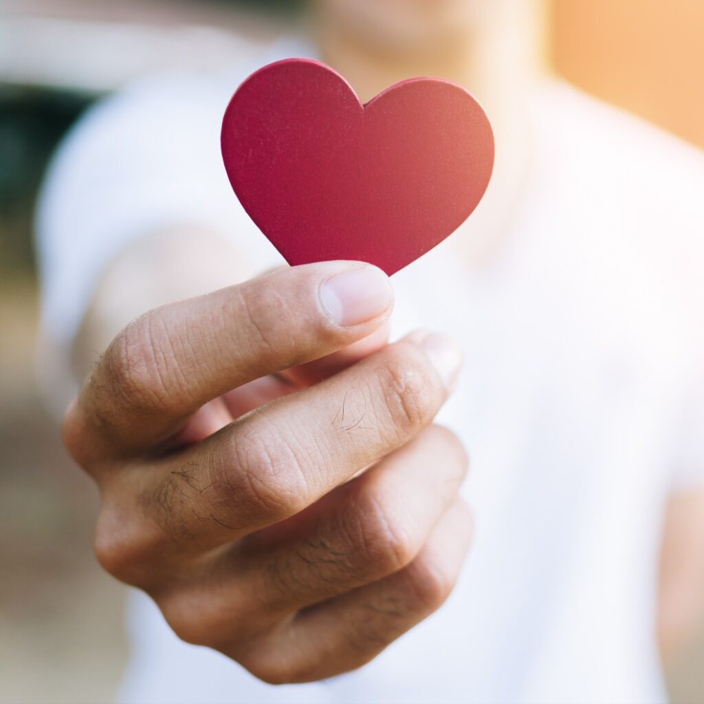 Asiatischer Mann hält rotes herzförmiges Holzstück mit verschwommenem Hintergrund